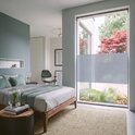 Slaapkamer met tweepersoonsbed en een groot raam met horizontale grijze vouwgordijnen.