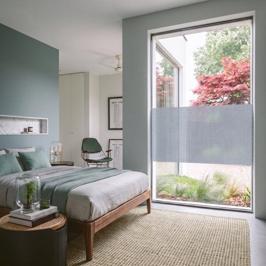 Slaapkamer met tweepersoonsbed en een groot raam met horizontale grijze vouwgordijnen.