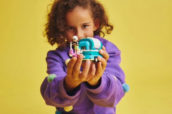 Kind houdt LEGO Friends bubbelthee kar met scooter en poppetje vast, met gele achtergrond.