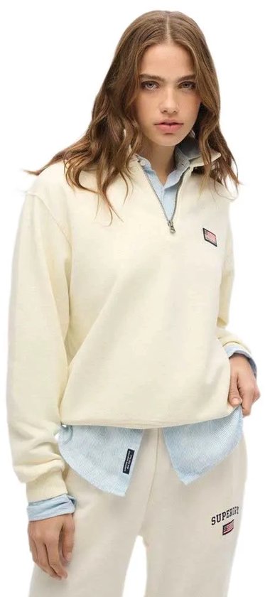 Model met een off-white, halve rits trui met kraag en een kleine Amerikaanse vlag badge op de linkerborst.
