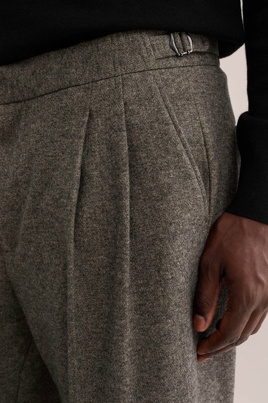 Detail van een grijze broek met dubbele bandplooien en een gesp aan de tailleband.