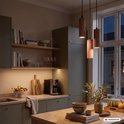 Drie verticale, geribbelde, koffiekleurige hanglampen boven een modern keukeneiland met groen-grijze kasten.