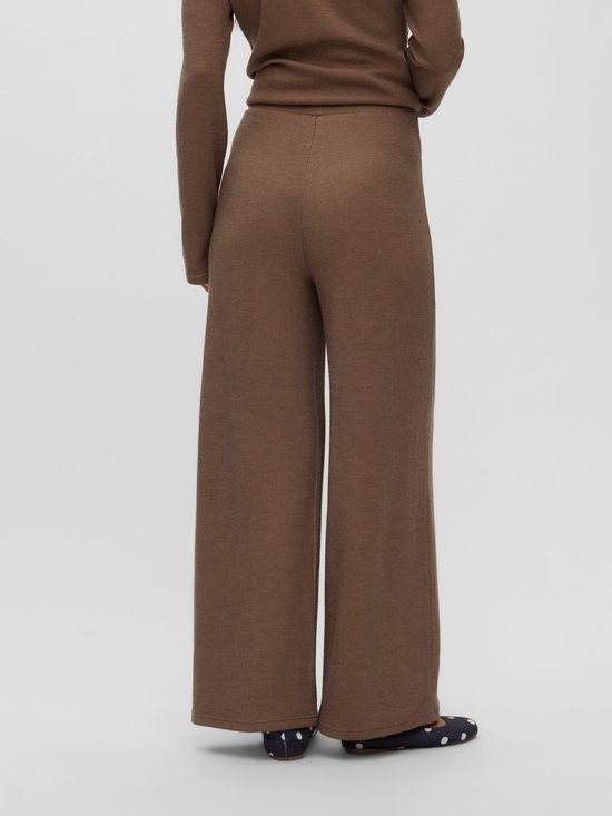 Achteraanzicht van een zwangere vrouw in een bruine, fijngebreide broek met wijde pijpen en bijpassende top.