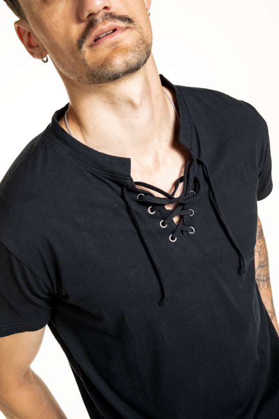 Close-up van een man met tattoos, draagt een zwart t-shirt met veterdetail.
