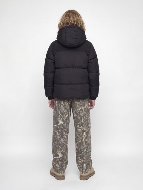Achterzijde van een zwarte gewatteerde jas met capuchon op een jongen met camouflagebroek.