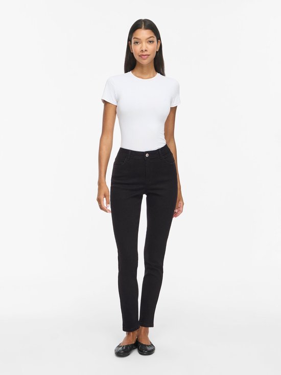 Model draagt een zwarte skinny jeans met middelhoge taille en een wit T-shirt.