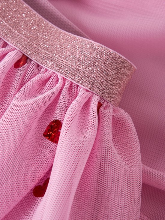 Close-up van roze tule stof met rode hartjes en een glitterende tailleband.