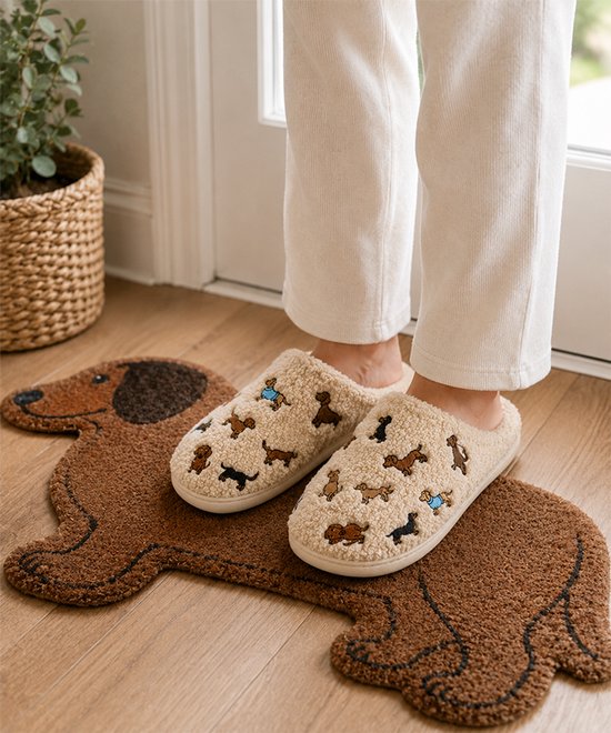Beige pantoffels met geborduurde teckels, liggend op een teckel-vormige deurmat.