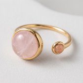 Close-up van een goudkleurige Lundholm ring met een grote roze rozenkwarts en een kleine zonnesteen.