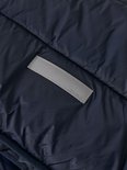 Detail van donkerblauwe, gewatteerde jas met een grijze reflecterende patch met "name it".