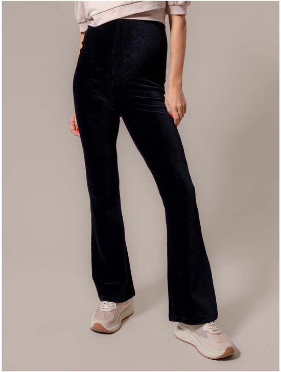 Zwangere vrouw draagt zwarte, uitlopende fluwelen zwangerschapsbroek met hoge taille en sneakers.