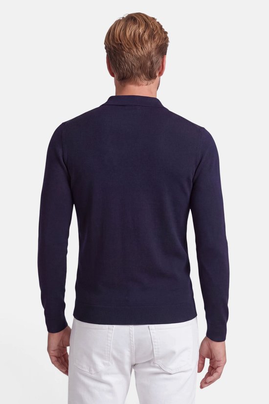 Achteraanzicht van een model in een marineblauwe polo met lange mouwen en een witte broek.