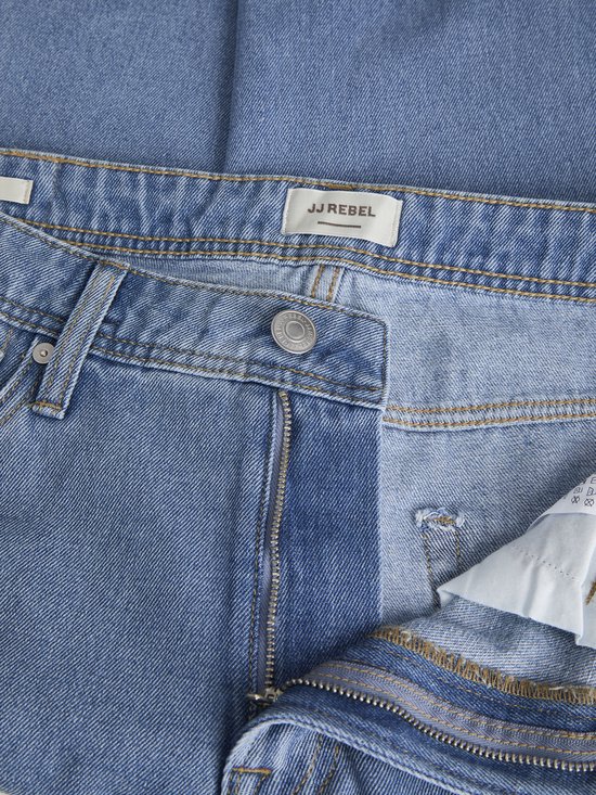 Detail van een lichtblauwe spijkerbroek met rits, knoop en het label 'JJ REBEL'.