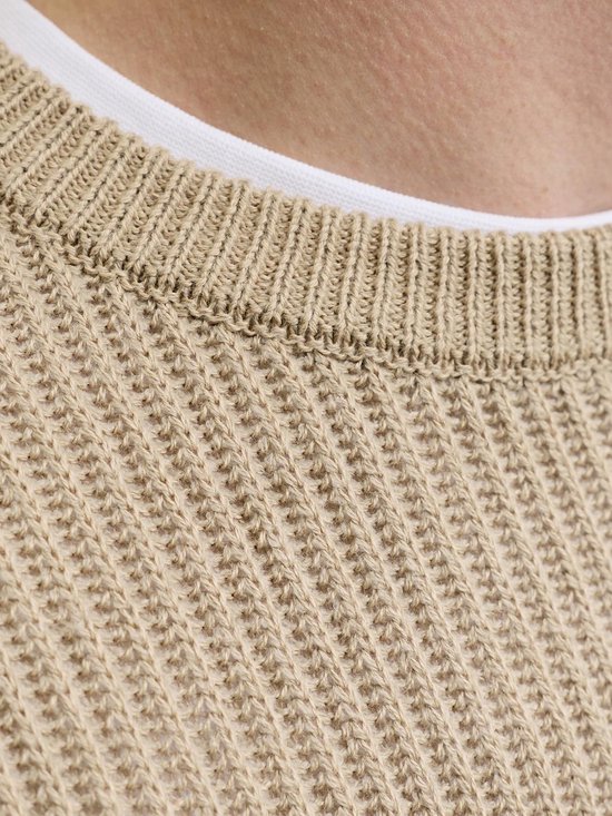 Close-up van een beige gebreide trui met een fijne ribbelstructuur en een witte onderlaag.