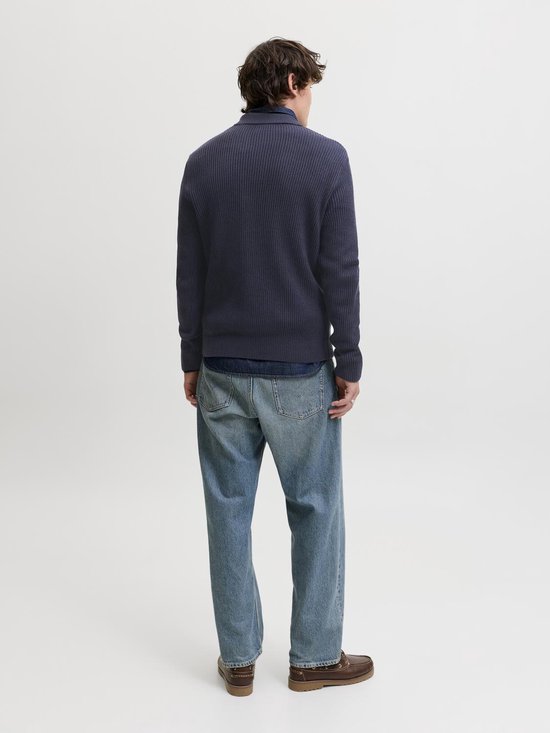 Man met lange mouwen, donkerblauwe gebreide polo, denim overhemd en spijkerbroek.