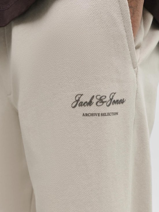 Detail van een beige joggingbroek met geborduurde 'Jack & Jones Archive Selection' tekst.