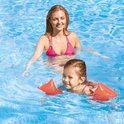 Vrouw met roze bikini en meisje met oranje zwembandjes om armen in blauw zwembad.