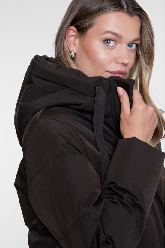Model met bruine lange pufferjas, met de hand bij de kraag en de capuchon.
