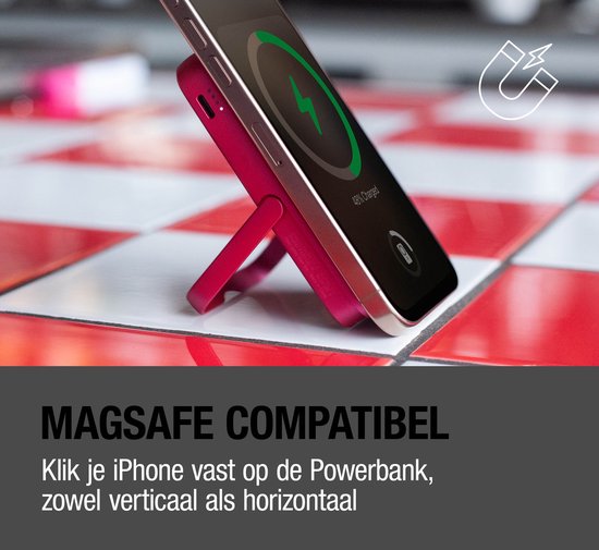 Een rode magnetische powerbank met ingeklapt standaardje laadt een iPhone op. De telefoon is verticaal bevestigd. Tekst: MAGSAFE COMPATIBEL.