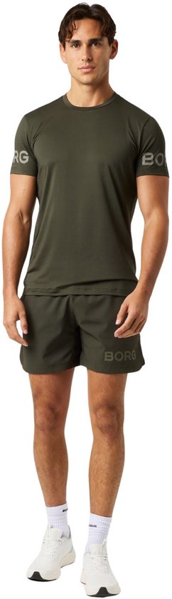 Man in een donkergroen sportshirt met logo op de mouwen en bijpassende donkergroene sportshort.