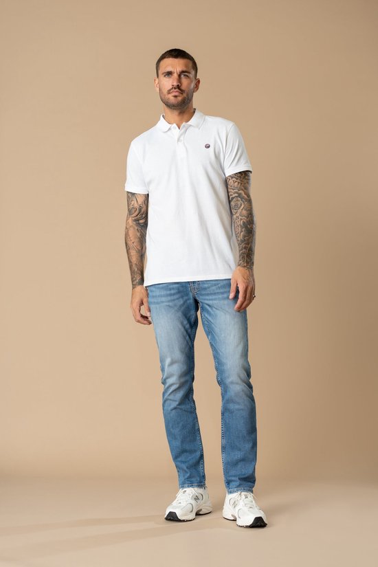 Man in witte polo en blauwe rechte jeans met witte sneakers.