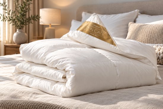 Opgevouwen wit donzen dekbed met gouden Ten Cate merklabel op een bed in een sfeervolle slaapkamer.