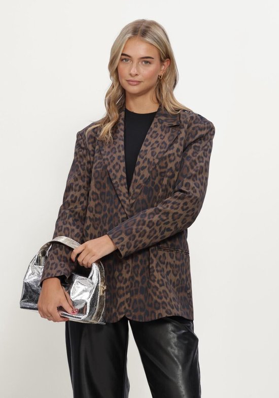 Model draagt een bruine blazer met luipaardprint, zwart shirt, lederen broek en houdt een zilveren handtas vast.