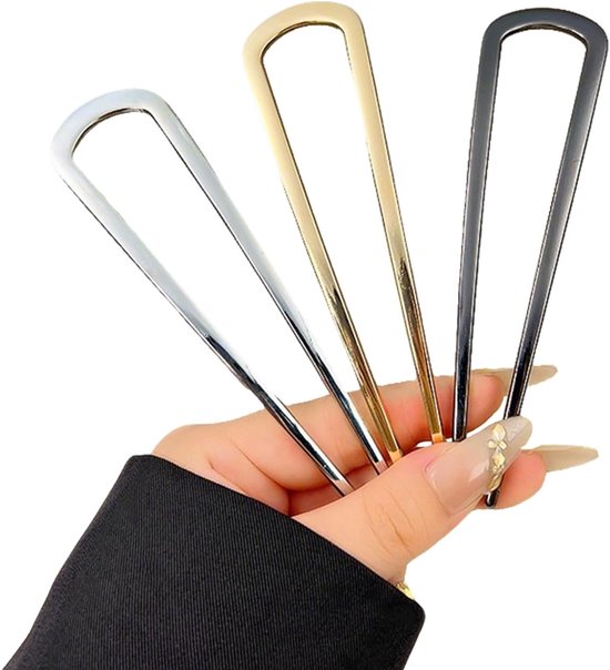 Drie U-vormige haarspelden in goud, zilver en zwart, vastgehouden in een hand.