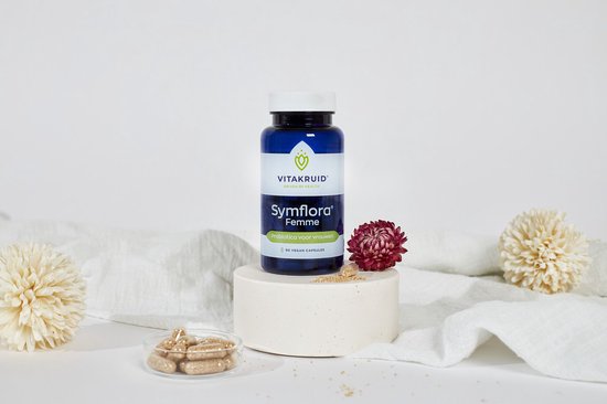 Blauwe Vitakruid Symflora Femme pot met 90 vegan capsules, op een voetstuk naast een bloem en schaaltje met capsules.