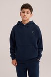 Jongen in een donkerblauwe hoodie met een wit vogelborduursel op de linkerborst.