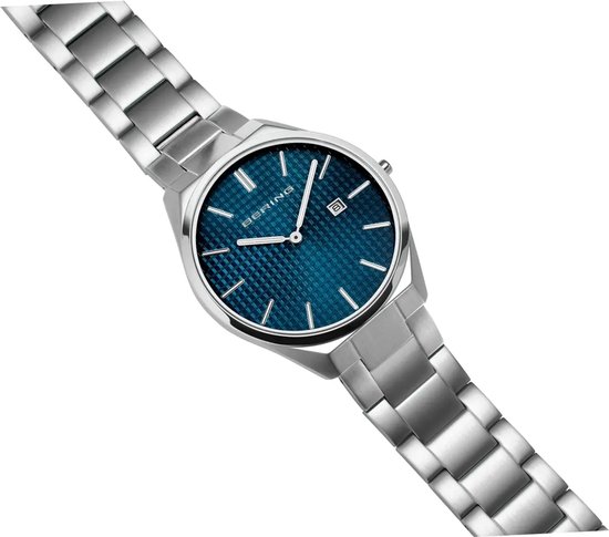 Zilverkleurig horloge met blauwe wijzerplaat met ruitpatroon en datumvenster, schuin van voren gefotografeerd.