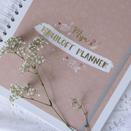 Close-up van een koraalkleurige ringband-planner met gouden tekst 'Myn Bruiloft Planner' en witte bloemen.