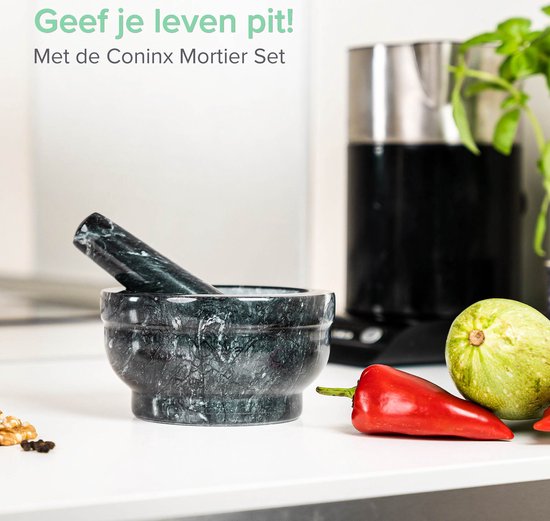 Zwart marmeren Coninx vijzel en stamper op een keukenblad met rode peper en courgette.