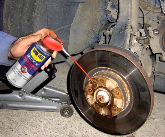 Hand spuit WD-40 Specialist Super Degrippant op een roestige remschijf van een auto.
