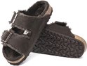 Een paar donkerbruine Birkenstock Arizona pantoffels, één van boven met gespen en lammenvacht, de andere van onder met profielzool.