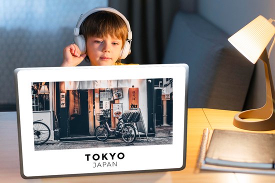 Un garçon avec un casque regarde un ordinateur portable affichant une scène de rue de Tokyo avec un vélo devant un restaurant.