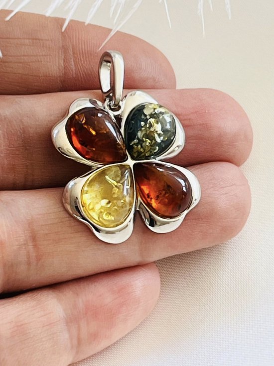 Klavertje vier hanger van zilver met vier stukken barnsteen in oranje, geel en groen, vastgehouden in een hand.