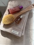Detail van een beige handdoek met een houten borstel, flesje olie en een ander flesje.