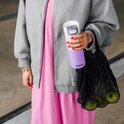 Vrouw met nagellak houdt een paarse Kambukka thermosbeker vast, naast een zwarte nettas met appels.