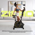 Vrouw poseert naast een zwarte hometrainer met gouden accenten, in een modern interieur.