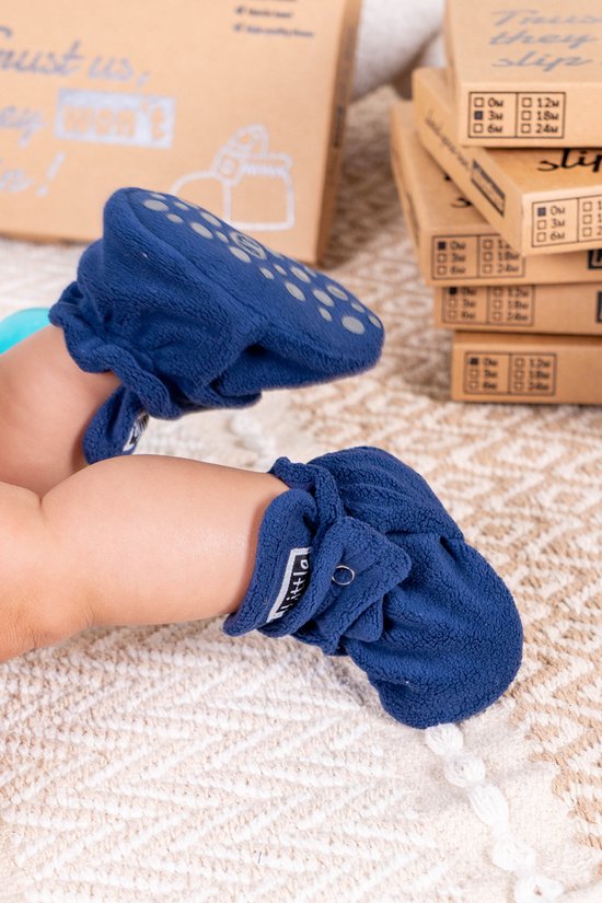 Een baby met donkerblauwe fleece Little Riots slofjes aan, met anti-slip zool zichtbaar.