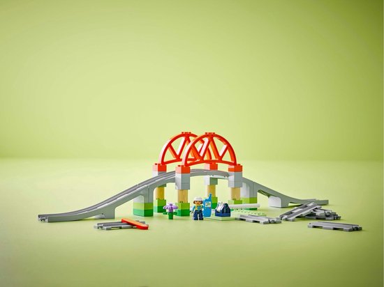 LEGO Duplo treinbaan met oranje bruggen, grijze rails, groene en beige steunen, en minifiguur.