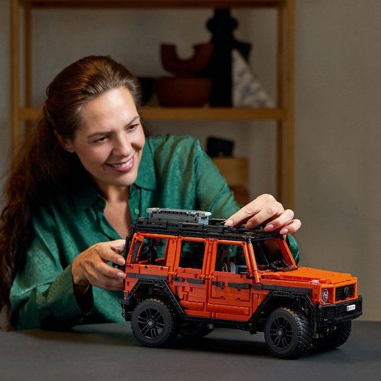 Een vrouw bouwt aan de oranje LEGO Technic Mercedes-Benz G 500 op een tafel.