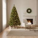 Kunstkerstboom met warme LED-lampjes, naast een open haard en een witte fauteuil.
