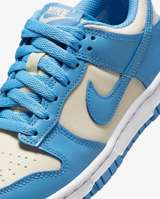 Detail van de Nike Dunk Low sneaker met crème en lichtblauwe leren overlays en blauwe veters.
