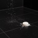 Witte douchetablet die oplost op een donkere douche vloer met opspattend water en schuim.