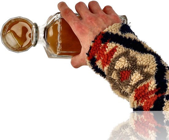 Een hand in een gebreide trui met patroon, die een glazen karaf met amberkleurige vloeistof en ijsklontjes vasthoudt.
