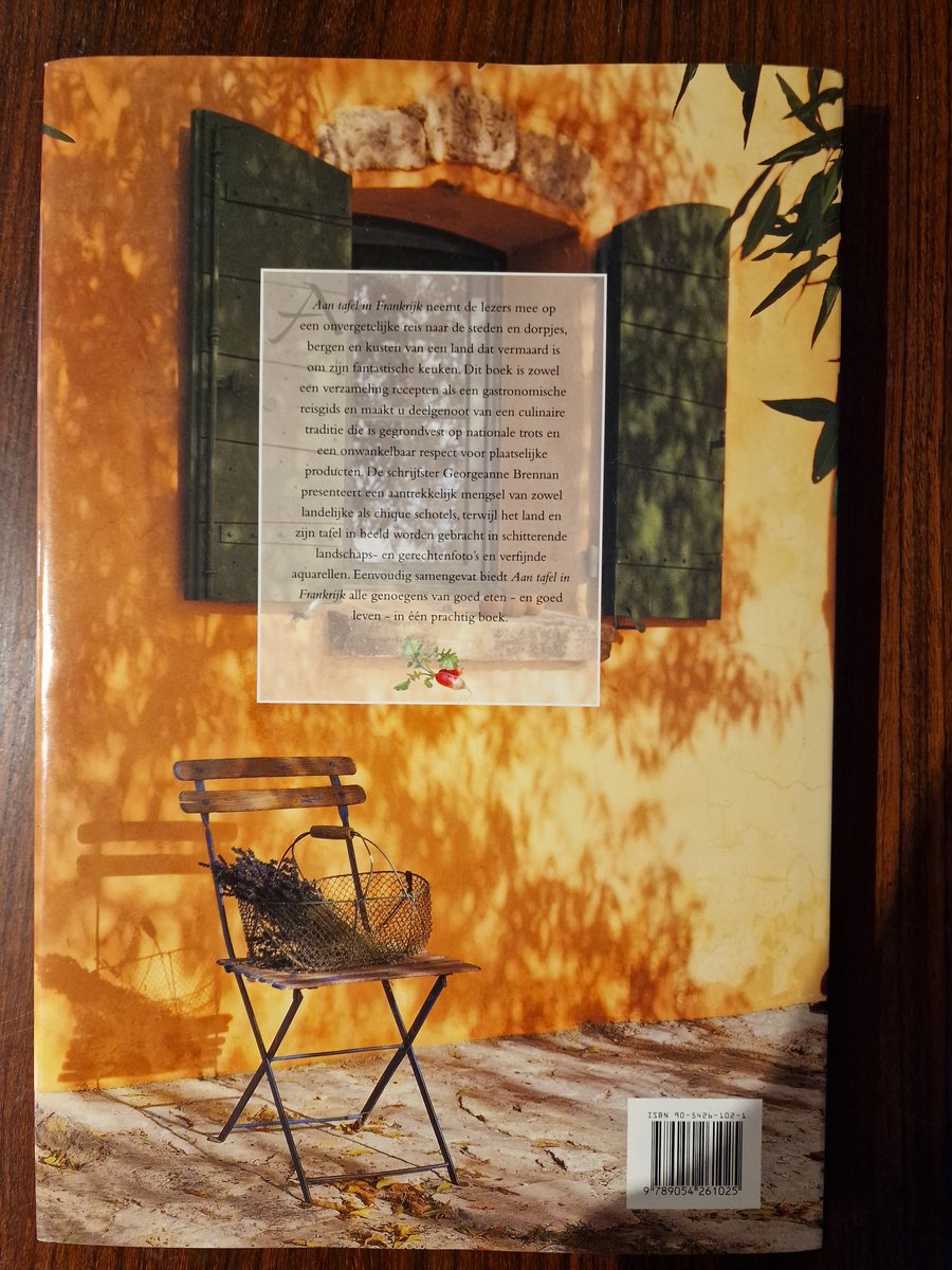 Achterkant van een boek met de titel "Aan tafel in Frankrijk", met tekst en een afbeelding van een stoel met droogbloemen.