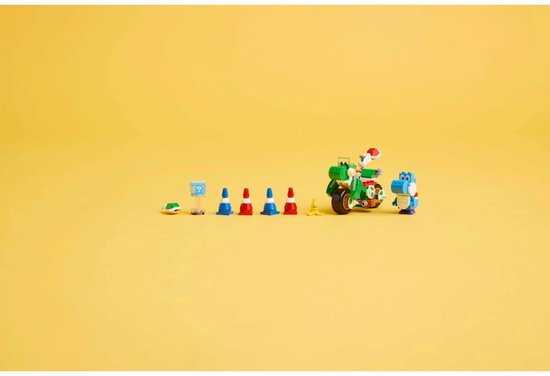 Een groene Lego-motor met een blauwe Yoshi, pionnen en een gele banaan op een gele achtergrond.