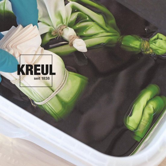 Main avec gant bleu plaçant du textile vert plié et noué dans un liquide sombre.